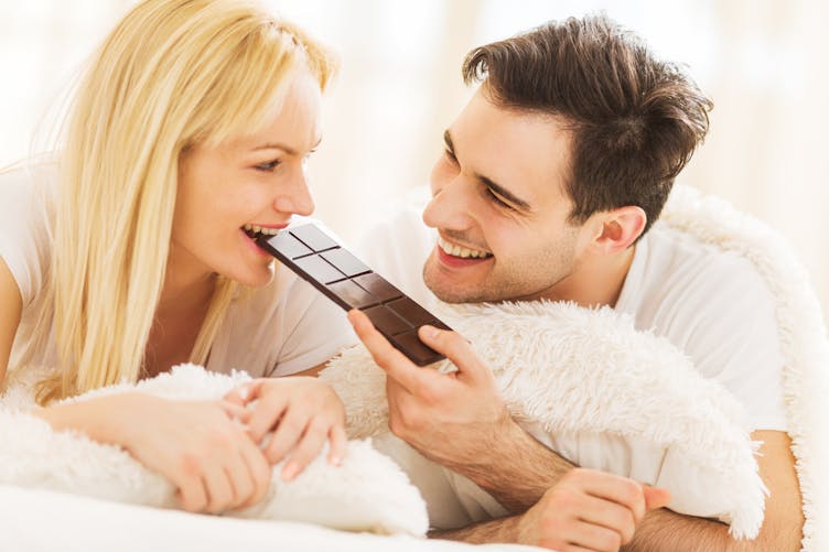 Couple au lit croquant une tablette de chocolat