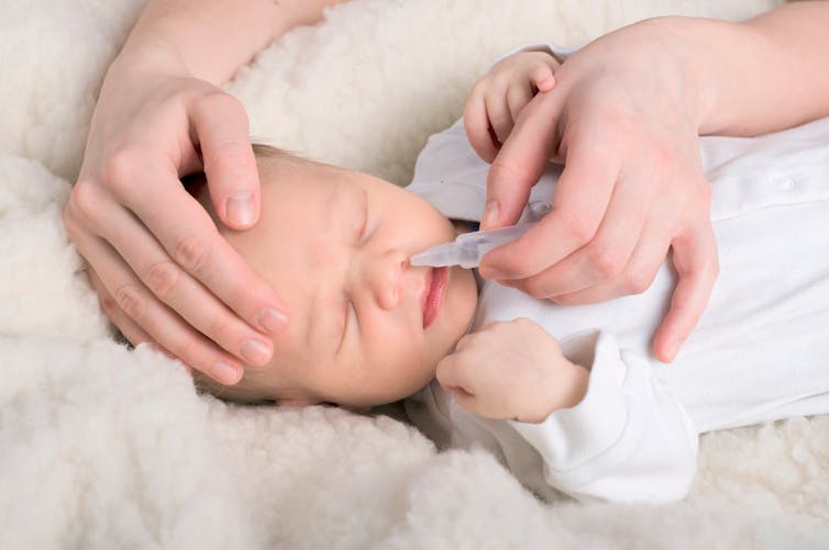 maman mettant du sérum physiologique dans le nez de bébé