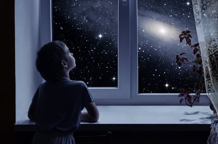 enfant regardant les étoiles par la fenêtre de sa chambre