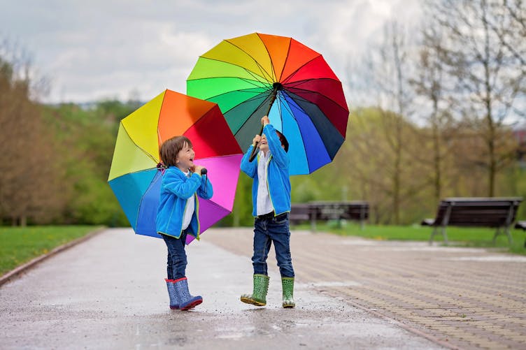 deux enfants jouent avec des parapluies dans un parc