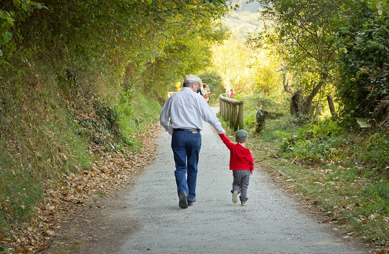 grand-père et son petit fils se promenant sur un chemin bordé d'arbres