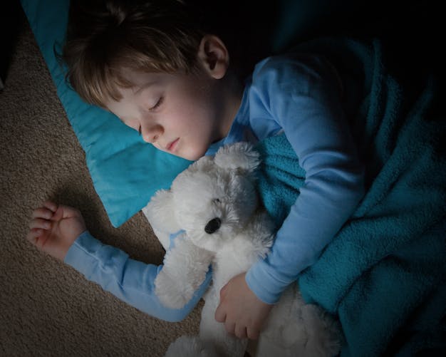 petit garçon dormant avec un ours en peluche dans les bras