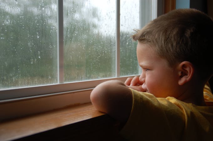 petit garçon regarde la pluie tomber par la fenêtre