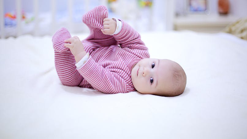 un bébé trop mignon les bras levé sur un lit