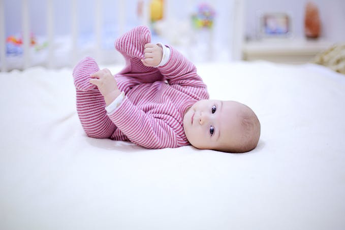 un bébé trop mignon les bras levé sur un lit