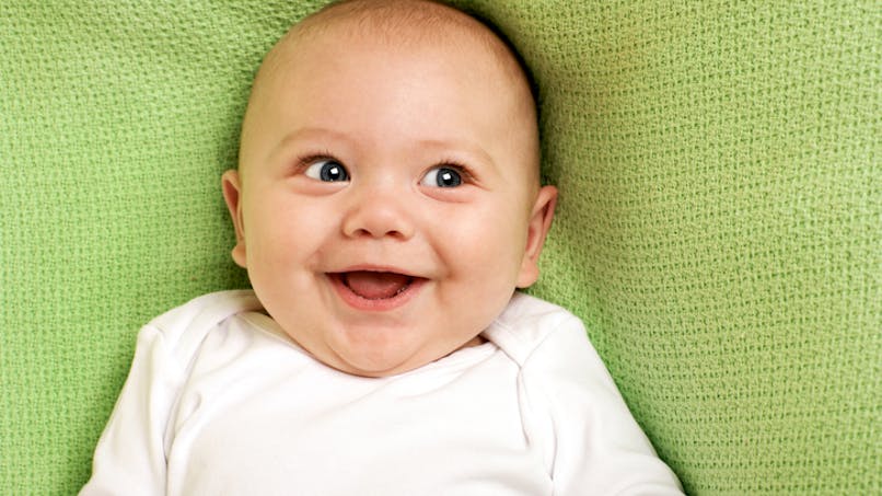 un bébé, qui rit, couché sur une couverture verte