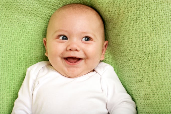 un bébé, qui rit, couché sur une couverture verte