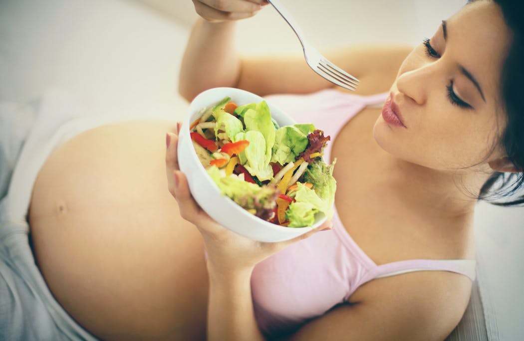 une femme enceinte mange une salade