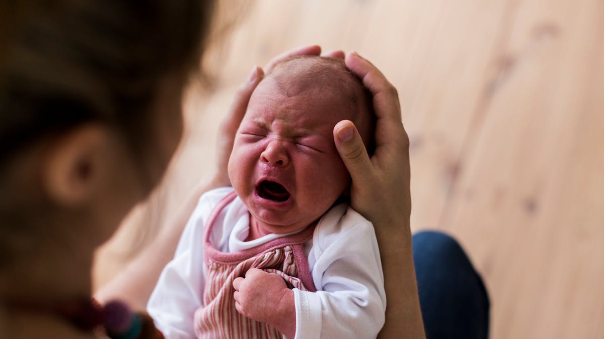 bébé qui pleure dans les bras de sa mère