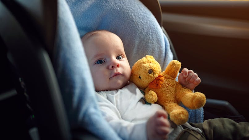 bébé dans siège auto tenant son doudou