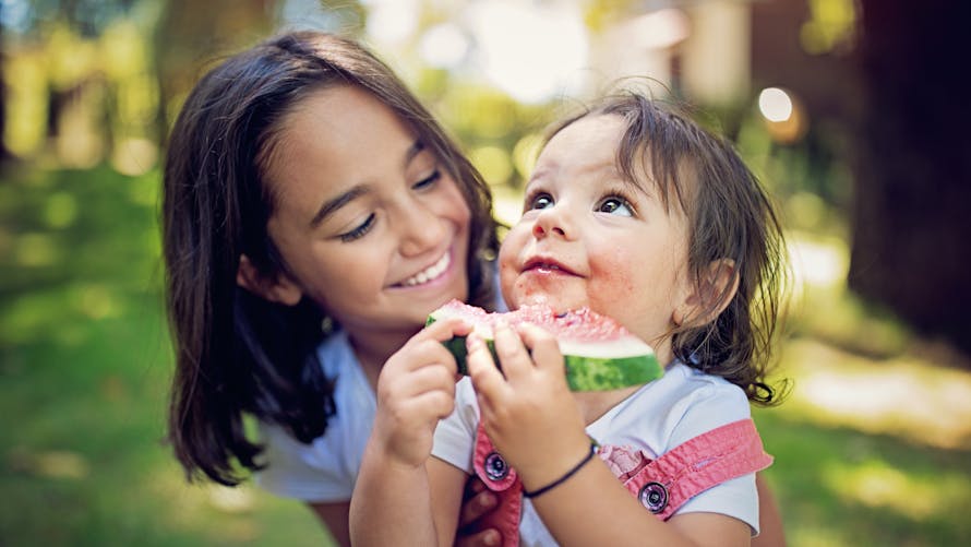 Alimentation bébé mois par mois : un enfant de 12 mois mange une pastèque avec sa grande soeur