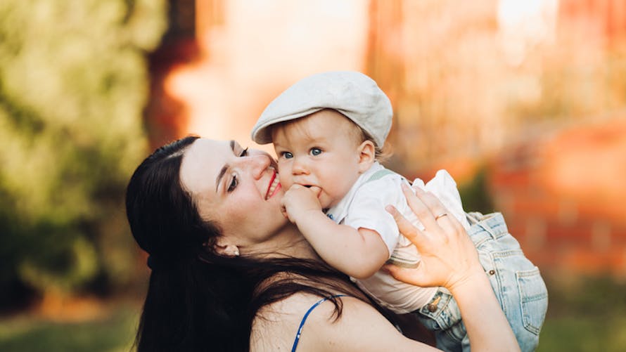 bébé portant une casquette, dans les bras de sa maman