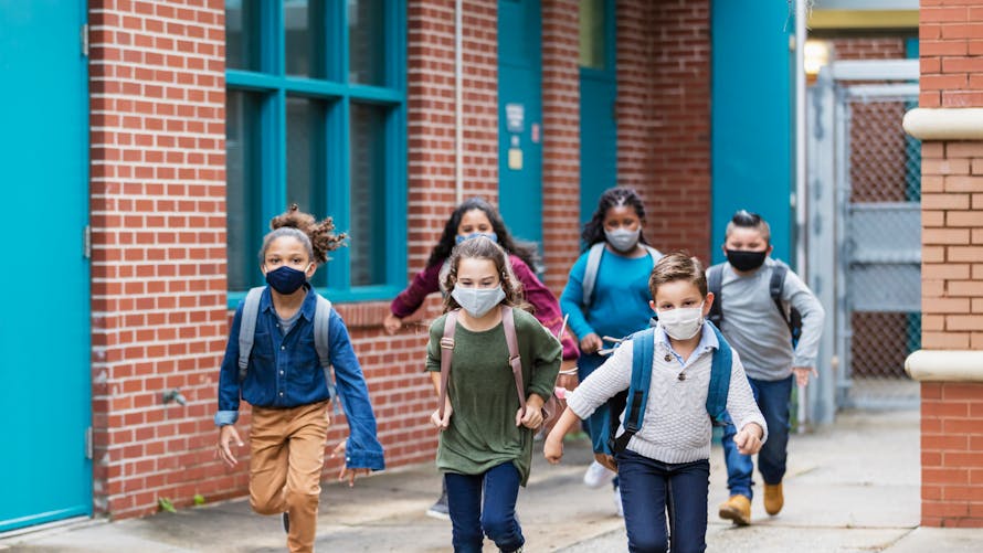 Des enfants courent en sortant de l'école primaire et portent des masques