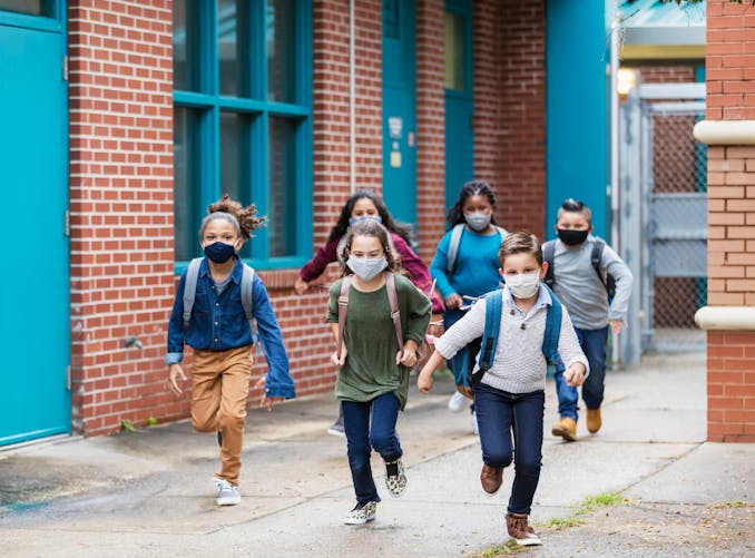 Des enfants courent en sortant de l'école primaire et portent des masques