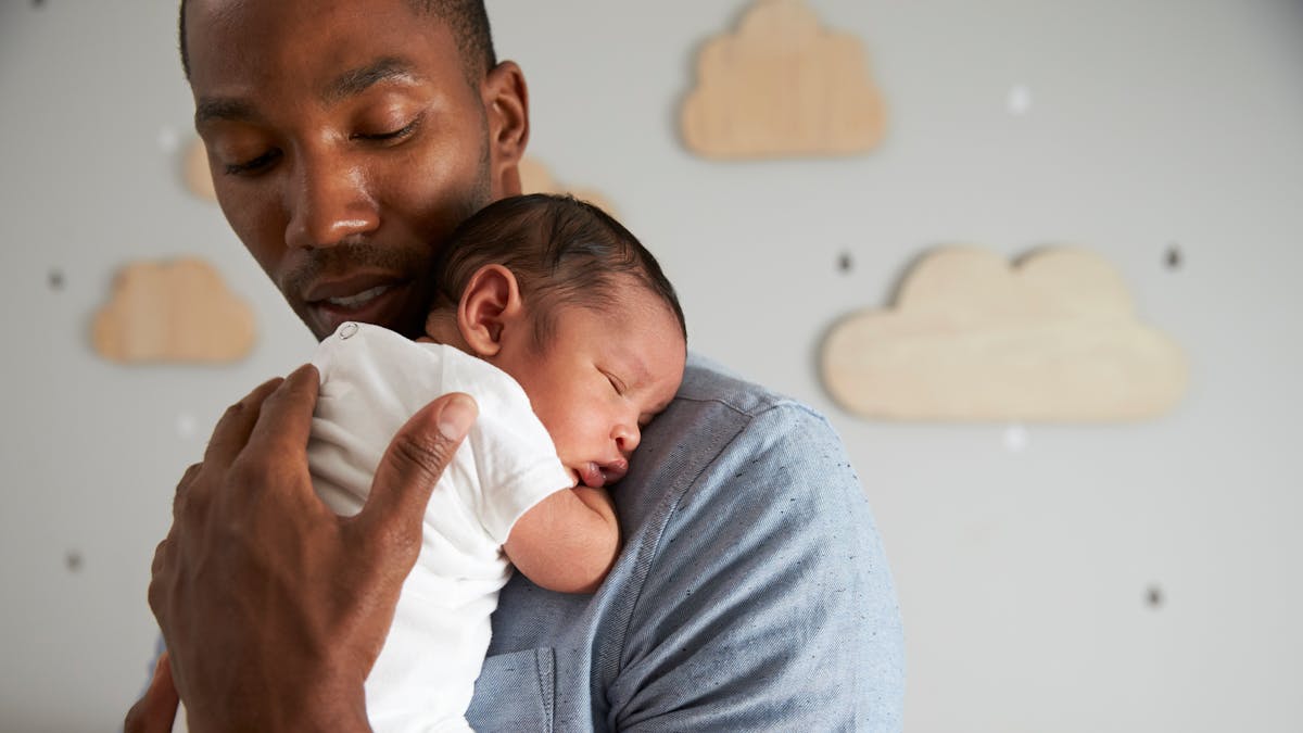 Un homme tient son nouveau-né endormi contre lui.