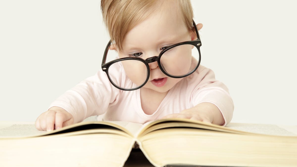 Un bébé avec des lunettes lit un grand livre.