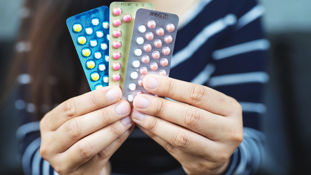 Une jeune femme montre trois plaquettes de pilules différentes
