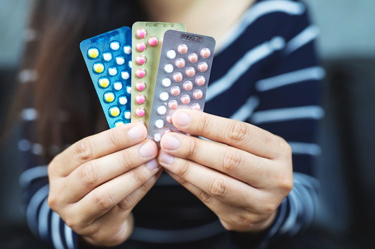Une jeune femme montre trois plaquettes de pilules différentes