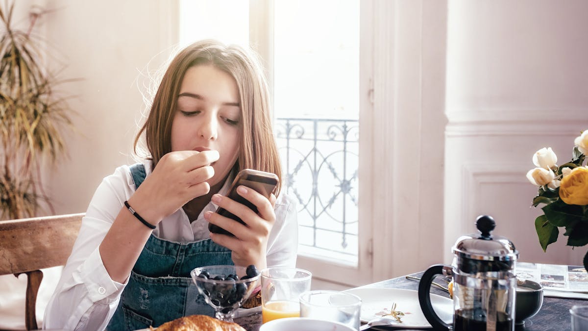 Une adolescente mange son petit-déjeuner devant son téléphone