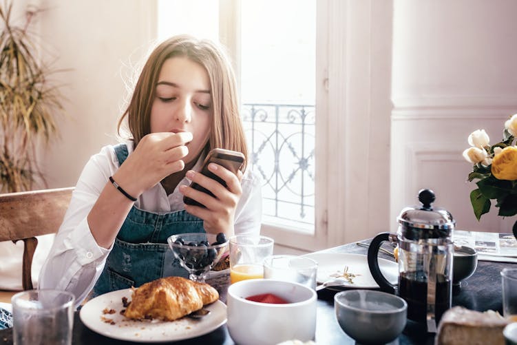 Une adolescente mange son petit-déjeuner devant son téléphone
