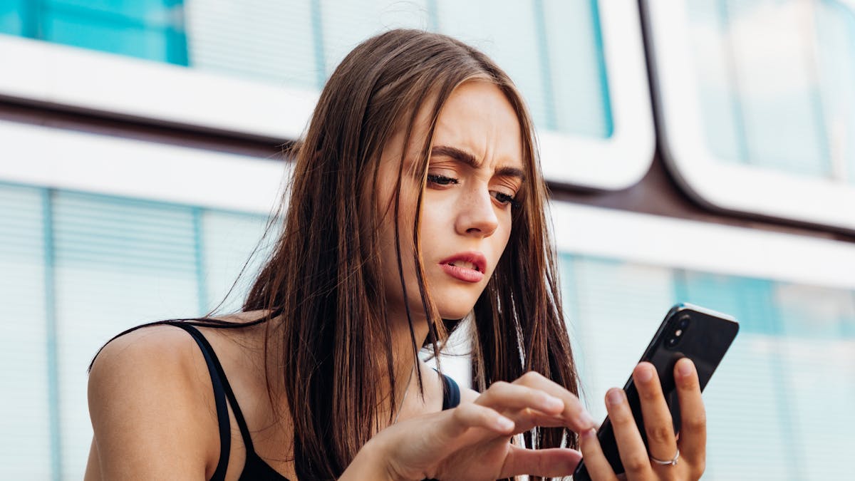 Une adolescente regarde, soucieuse, son téléphone.