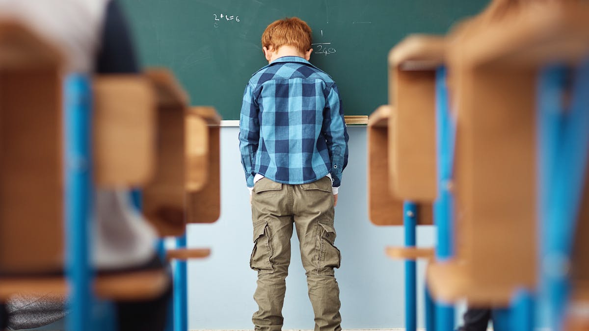 Un enfant, tête contre le tableau de sa classe, semble mal à l'école.
