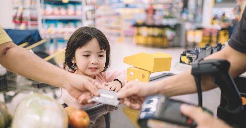 Une petite fille regarde son parent donner sa carte bancaire au caissier.