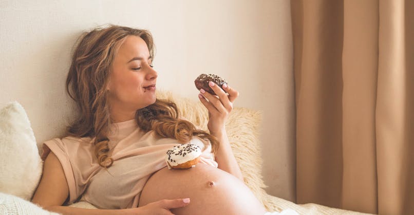 Une femme enceinte mange des donuts.