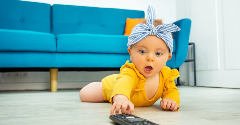 Un bébé s'approche d'une télécommande, contenant une pile. 