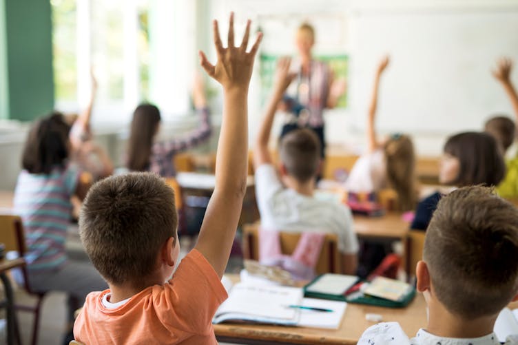 Enfants qui lèvent la main dans une classe.