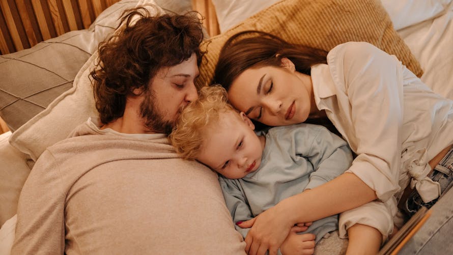 Deux parents qui dorment avec un bébé au mileu. 
