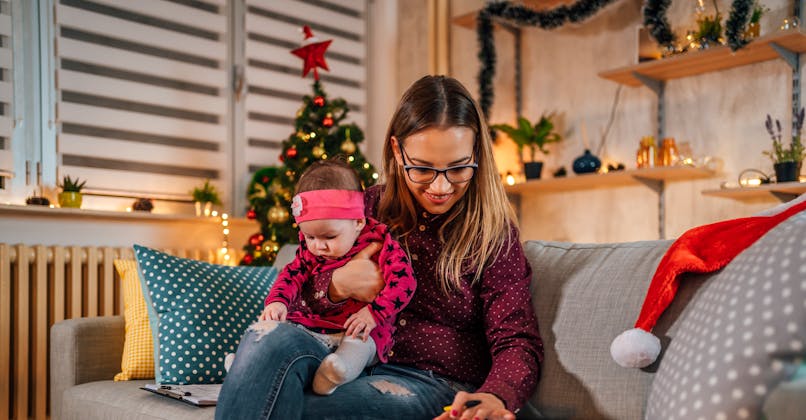 Une maman calcule son budget de Noël avec son bébé sur les genoux.