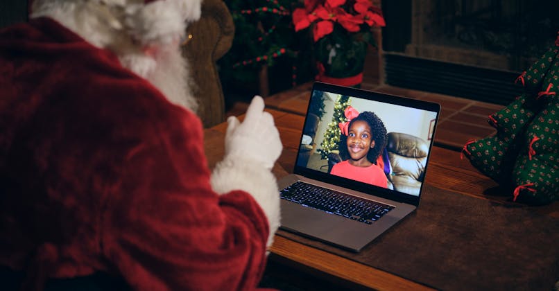 Un père Noël qui passe un appel en visio avec une jeune fille sur son ordinateur. 