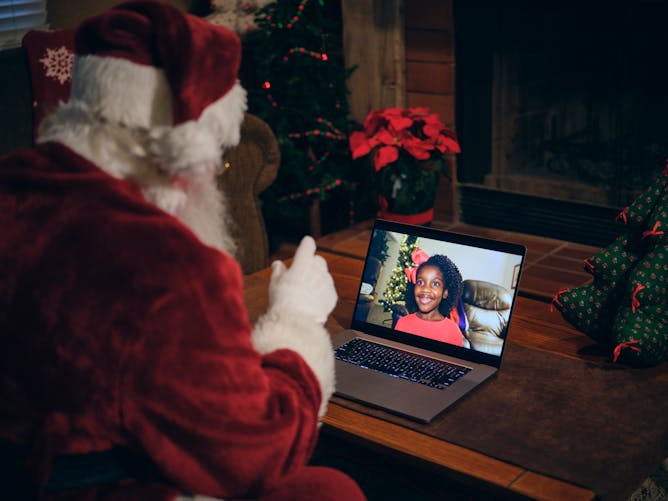 Un père Noël qui passe un appel en visio avec une jeune fille sur son ordinateur. 