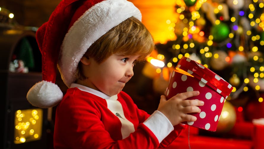 Un petit garçon déguisé en Père Noël ouvre son cadeau.