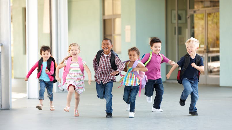 Des enfants avec des sacs-à-dos courent vers leur école.
