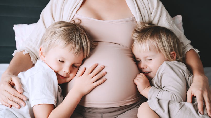 Deux enfants sont blottis contre le ventre de leur maman, enceinte.