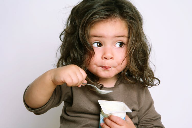 Une enfant mange un yaourt.