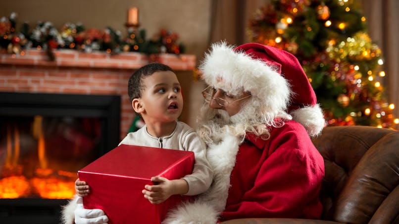 Un enfant sur les genoux du Père Noël reçoit un cadeau.