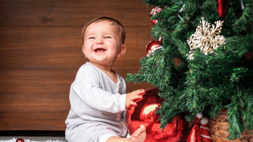 Un bébé souriant devant un sapin de Noël décoré