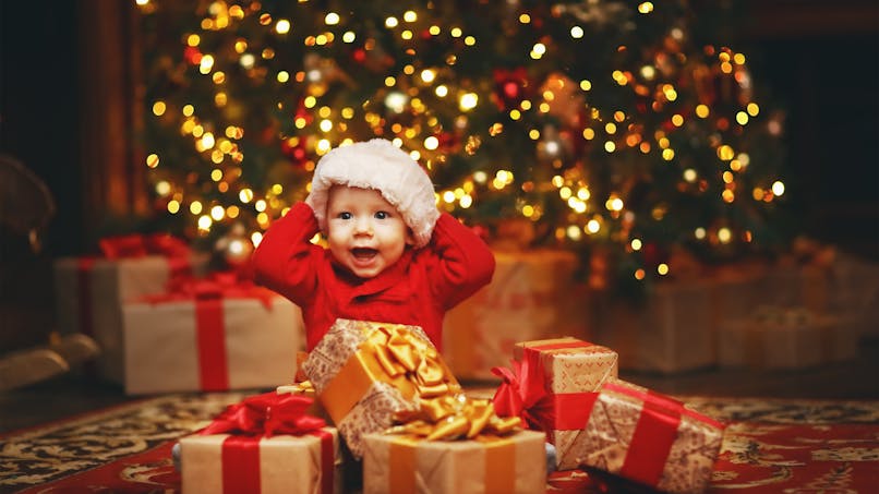 Un bébé devant un sapin et des cadeaux de Noël