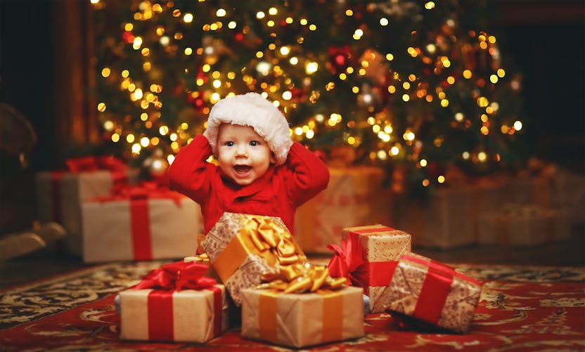 Un bébé devant un sapin et des cadeaux de Noël