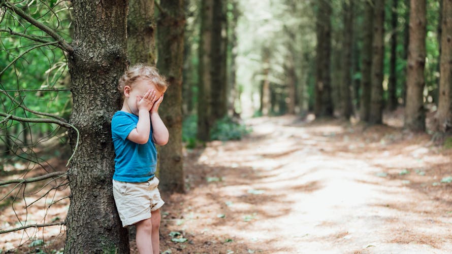 Un enfant joue à cache-cache en forêt