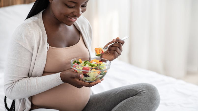 Une femme enceinte mange une salade de crudités.