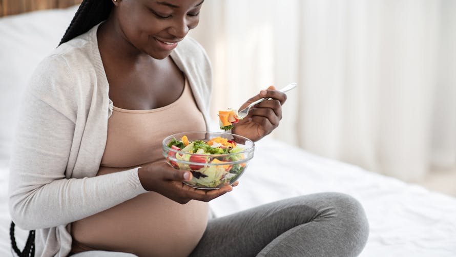 Une femme enceinte mange une salade de crudités.