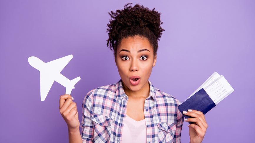 Une femme tenant un petit avion et son passeport exprime de la surprise.