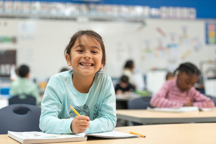 Une enfant souriante est à l'école, crayon à la main.