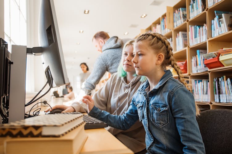Deux jeunes filles travaillent sur un ordinateur dans une bibliothèque scolaire.