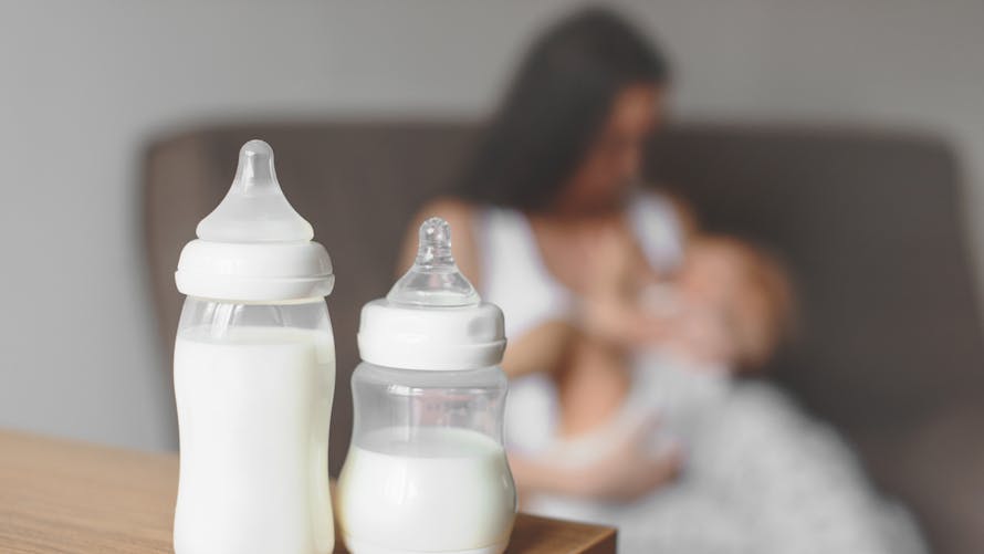 Bouteilles de lait maternel sur le fond de la mère tenant dans ses mains et le bébé allaité