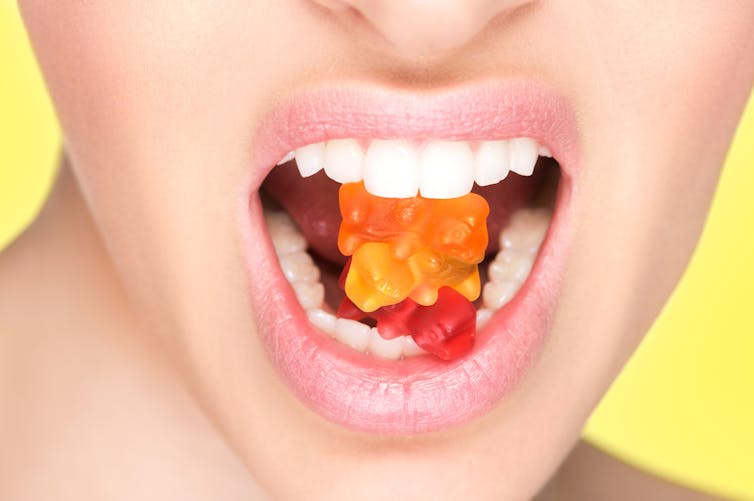 Une femme croque à pleines dents de petits bonbons de type gummies